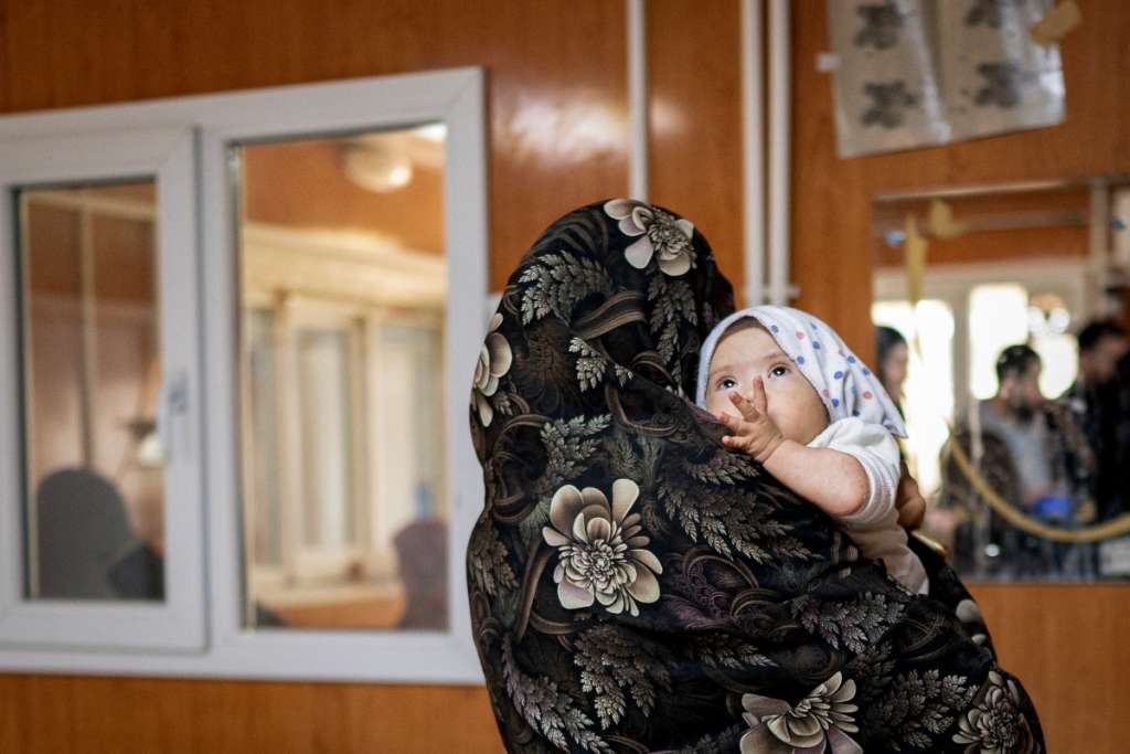 TOPSHOT - This photograph taken on January 8, 2026 shows Jamila, an Afghan woman, carrying her eight-month-old daughter after an interview with AFP in the Medecins Sans Frontieres (MSF) centre at a hospital in Herat.