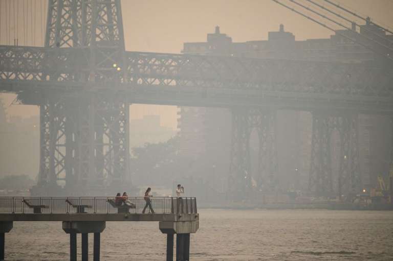 Varias personas en un muelle ante el horizonte de la ciudad de Nueva York y el East River envueltos en humo, en Brooklyn, el 5 de junio de 2023. El humo de los cientos de incendios forestales que arrasan el este de Canadá se ha desplazado hacia el sur.