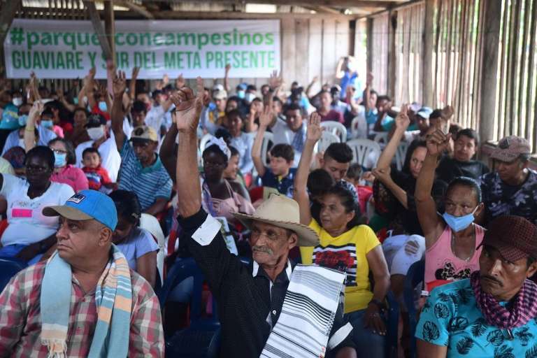 un grupo de personas campesinas que se encuentran reunidas, levantan al tiempo la mano