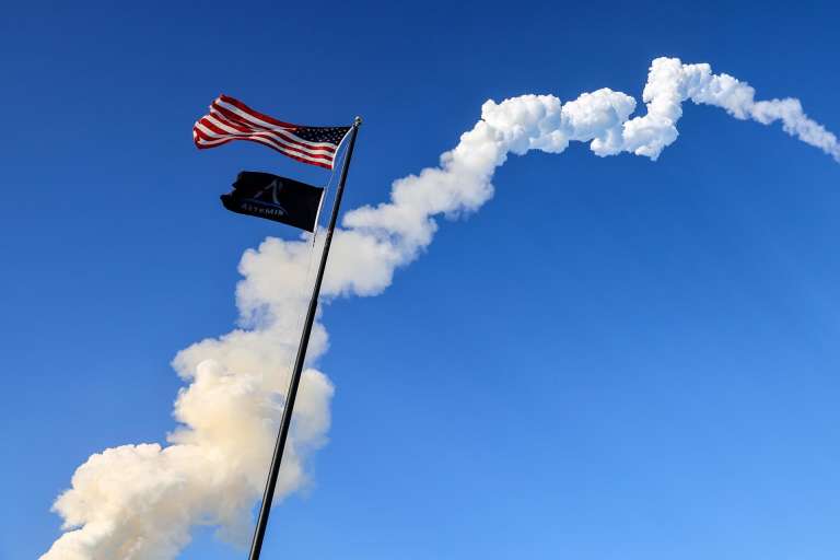 TITUSVILLE (United States), 02/04/2026.- The US flag flutters in the wind as the trail of the Space Launch System (SLS) rocket carrying the Orion capsule for the Artemis II mission crosses the sky after launch from Launch Pad 39B at the Kennedy Space Center in Titusville, Florida, USA, 01 April 2026. The crew includes NASA astronauts Reid Wiseman, commander, Victor Glover, pilot, Christina Koch, mission specialist, and Canadian Space Agency (CSA) astronaut Jeremy Hansen, mission specialist. The mission will conduct a crewed flyby of the Moon, the first human flight beyond low Earth orbit since 1972. EFE/EPA/CRISTOBAL HERRERA-ULASHKEVICH