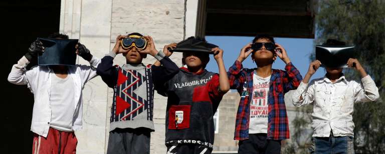 Los niños usan gafas protectoras y placas de rayos X para observar un eclipse solar parcial en Sana'a, Yemen.