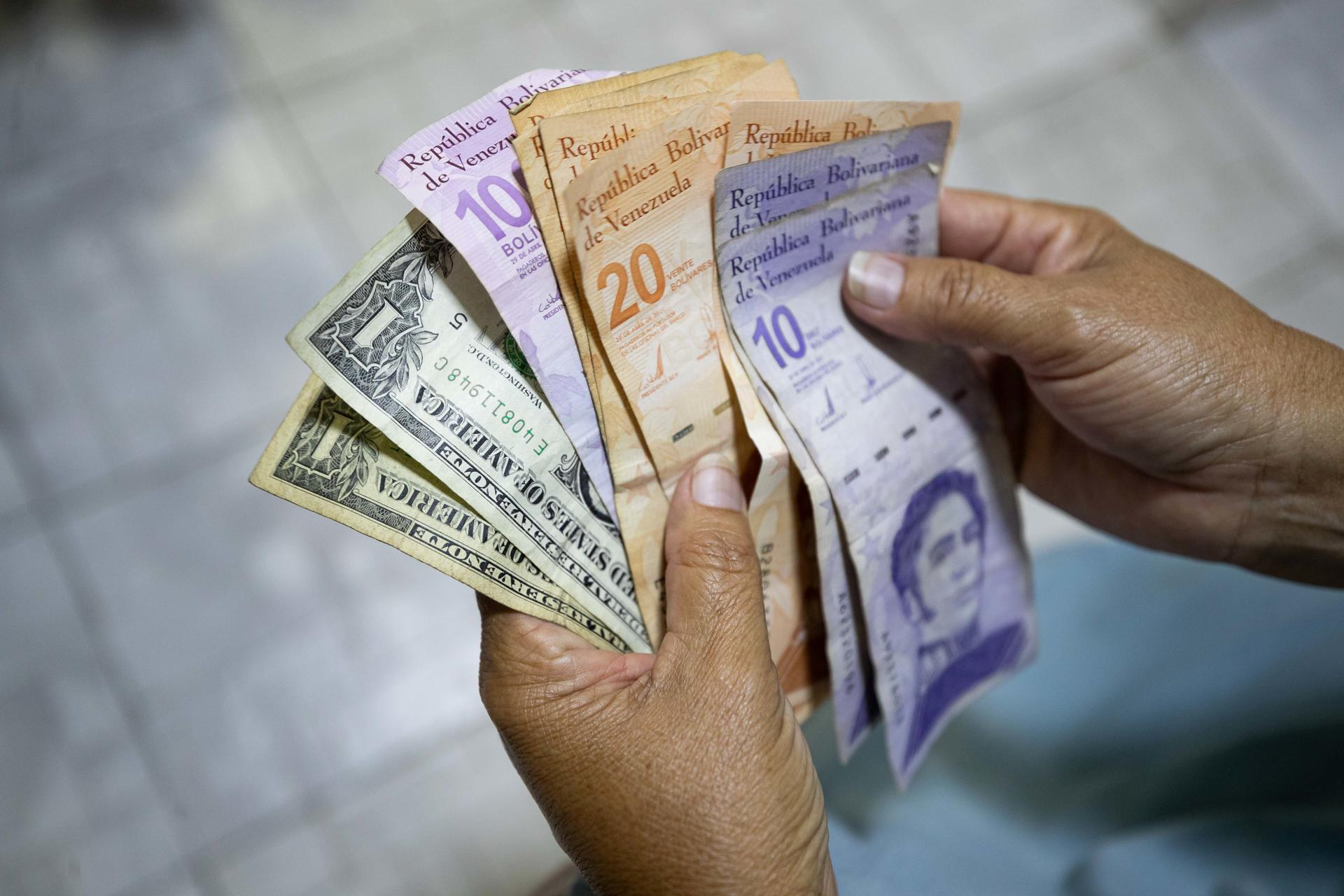 AME3872. CARACAS (VENEZUELA), 19/07/2025.- Una persona muestra billetes de bolívares y dólares este viernes, en Caracas (Venezuela). Venezuela, al cierre del primer semestre, mantiene a flote la producción petrolera, pese a las sanciones estadounidenses, pero aún enfrenta debilidades en materia cambiaria, inflación y salarios, especialmente los pagados en bolívares, la moneda nacional, que siguió devaluándose frente al dólar, el principal indicador de precios en el país. EFE/ Ronald Peña R
