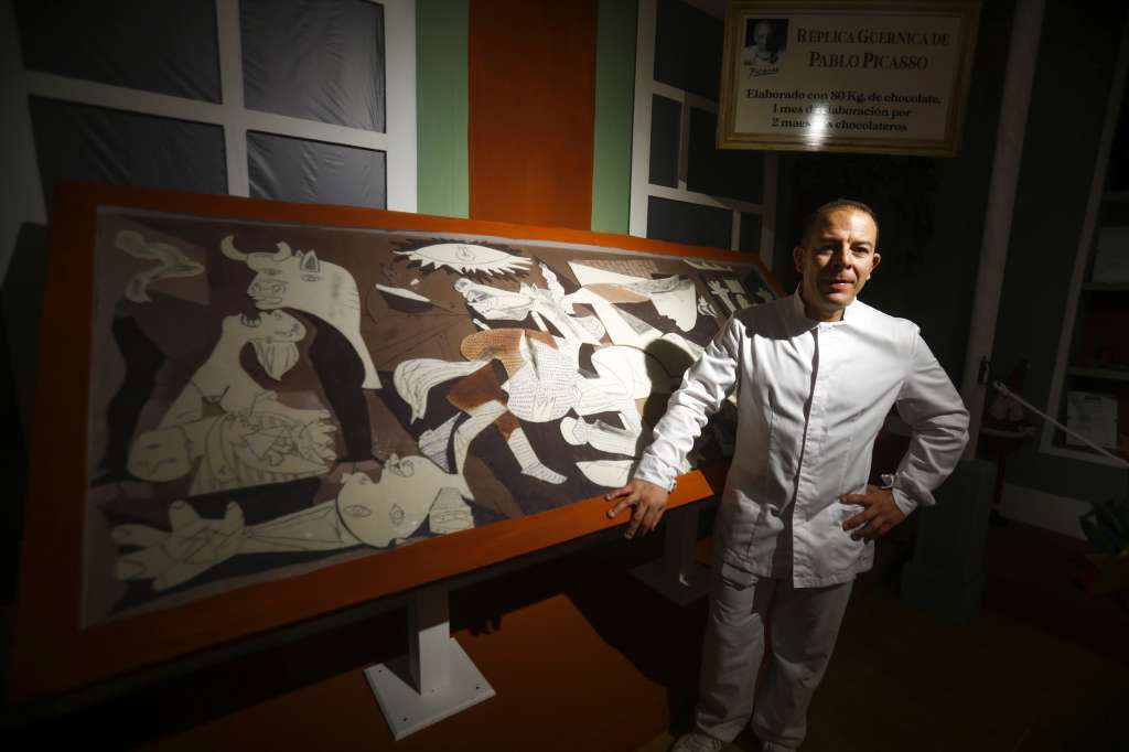 -FOTODELDIA- RUTE (CÓRDOBA), 24/12/2022.- Jorge Garrido posa junto al cuadro del Guernica elaborado con chocolate en el obrador Galleros Artesanos de Rute (Córdoba). El obrador, famoso por su tradicional Belén de Chocolate, ha elaborado su particular visión del Guernica de Pablo Picasso en chocolate negro y blanco para rendir un dulce homenaje a la figura del genial pintor malagueño, cuyo 50 aniversario de su muerte se celebra en 2023. EFE/Salas