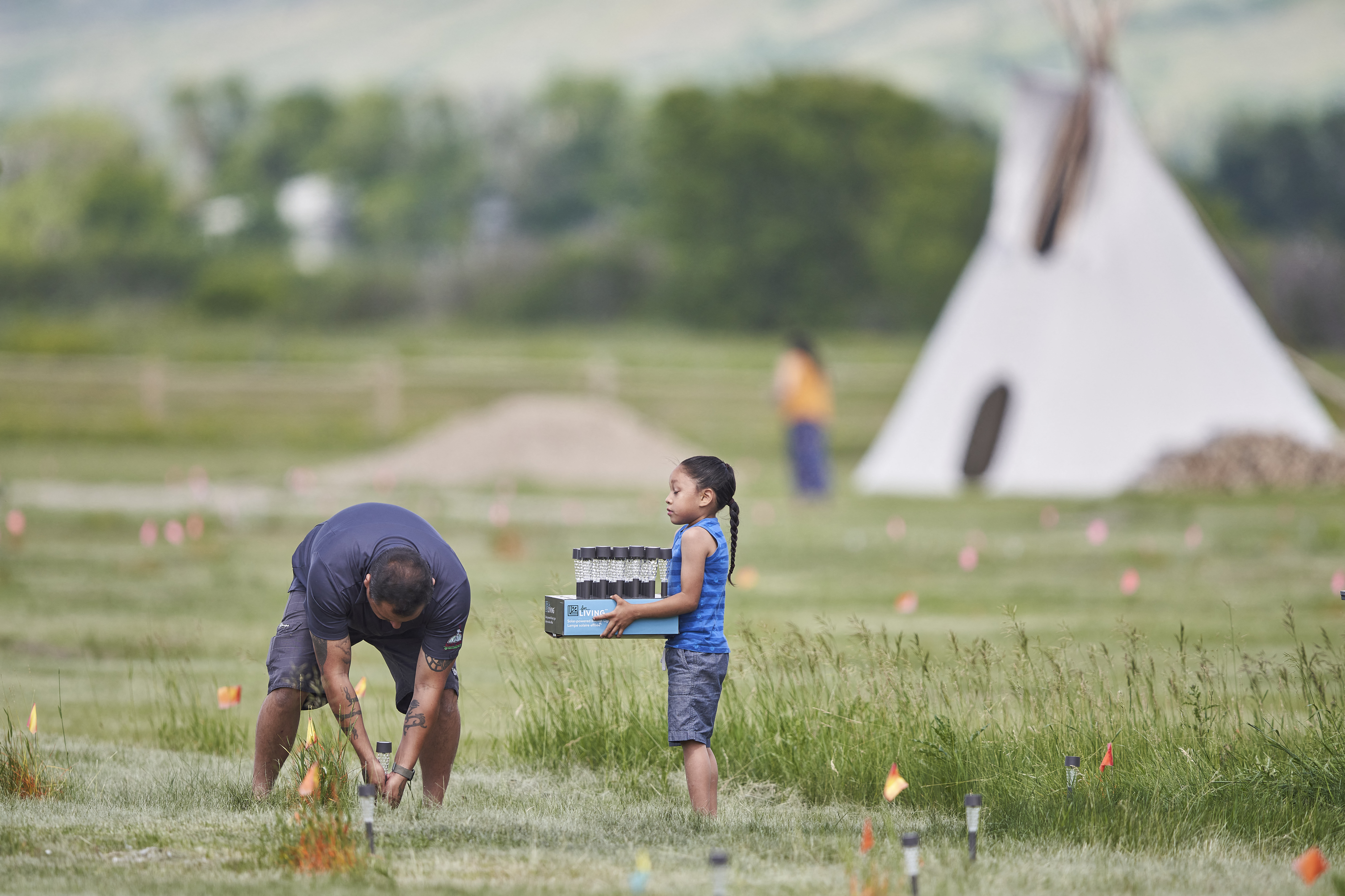 Miembros de la comunidad colocan luces solares junto a las banderas que marcan los lugares donde se han encontrado, en los últimos días, algunos de los restos de niños indígenas en Canadá.