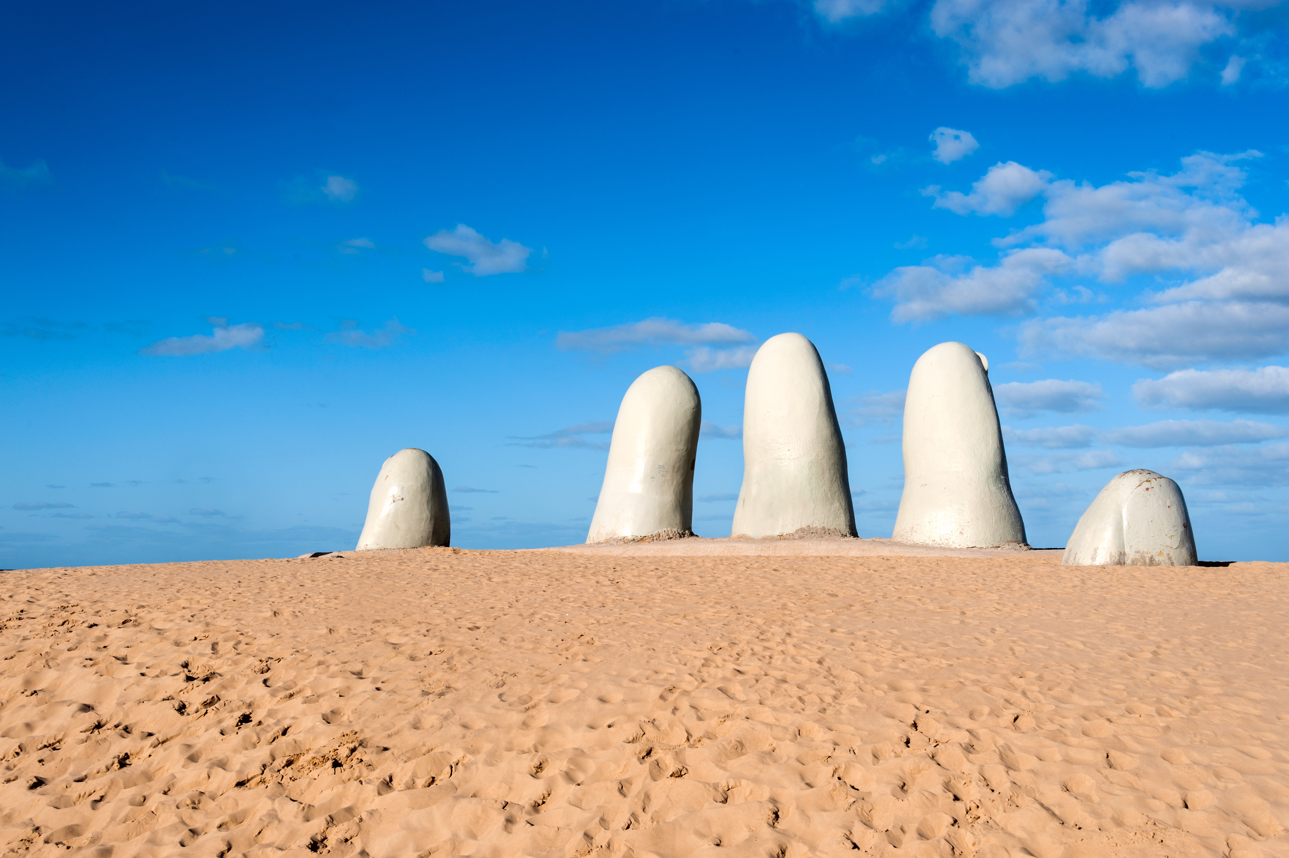 Escultura de los dedos en Uruguay
Cuenta la leyenda que los deseos de aquellos enamorados que se besen sobre la mano de Playa Mansa se cumplirán si son sinceros. Ubicada en la costa de Río de la Plata, Maldonado, se ha convertido en unos de los principales puntos de interés para aquellos que buscan una escapada tranquila y romántica entre arena fina y olas de pequeño tamaño.
De camino a la mano bajo la playa, es parada obligatoria el Faro, la construcción más antigua de la península , los enormes nidos de amor de San Rafael y los característicos puentes ondulantes.