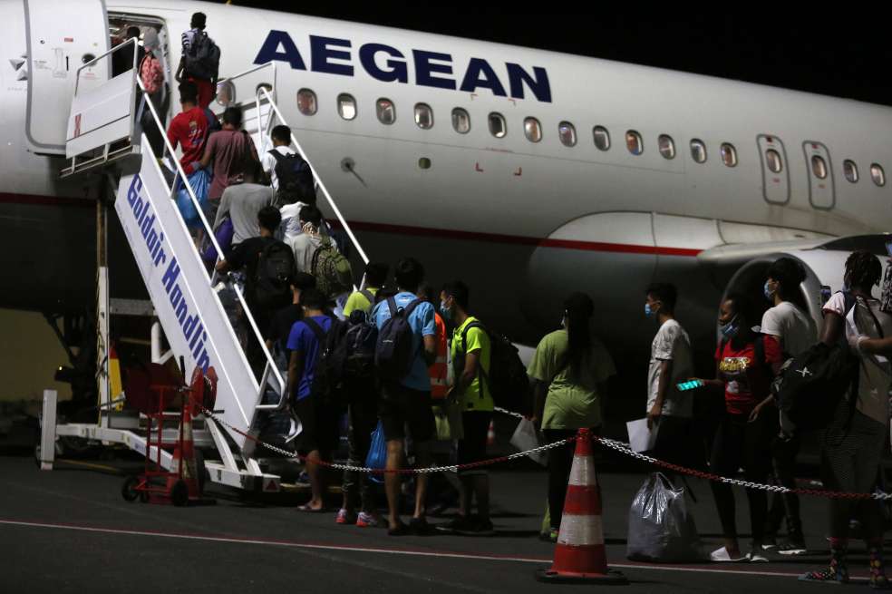 Decenas de migrantes hacen fila para ingresar a un avión.