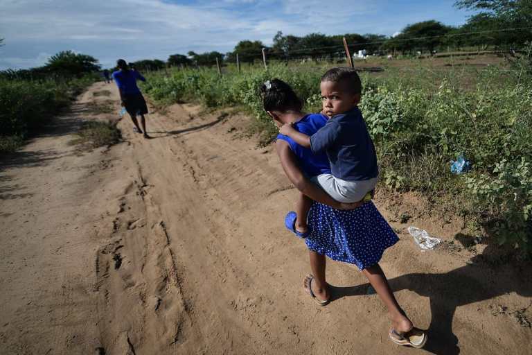 Una niña camina con un bebé en la espalda