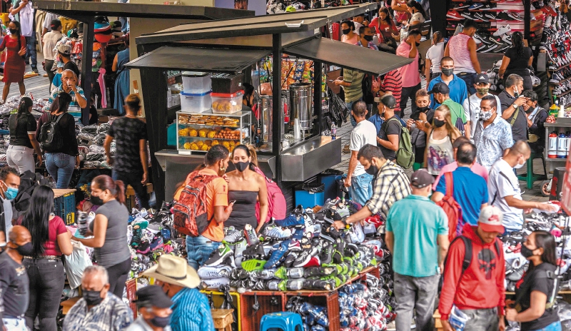 People walk around as street vendors interact with clients amid the Covid-19 pandemic, on a street in Medellin, Colombia, on December 17, 2020. / AFP / JOAQUIN SARMIENTO