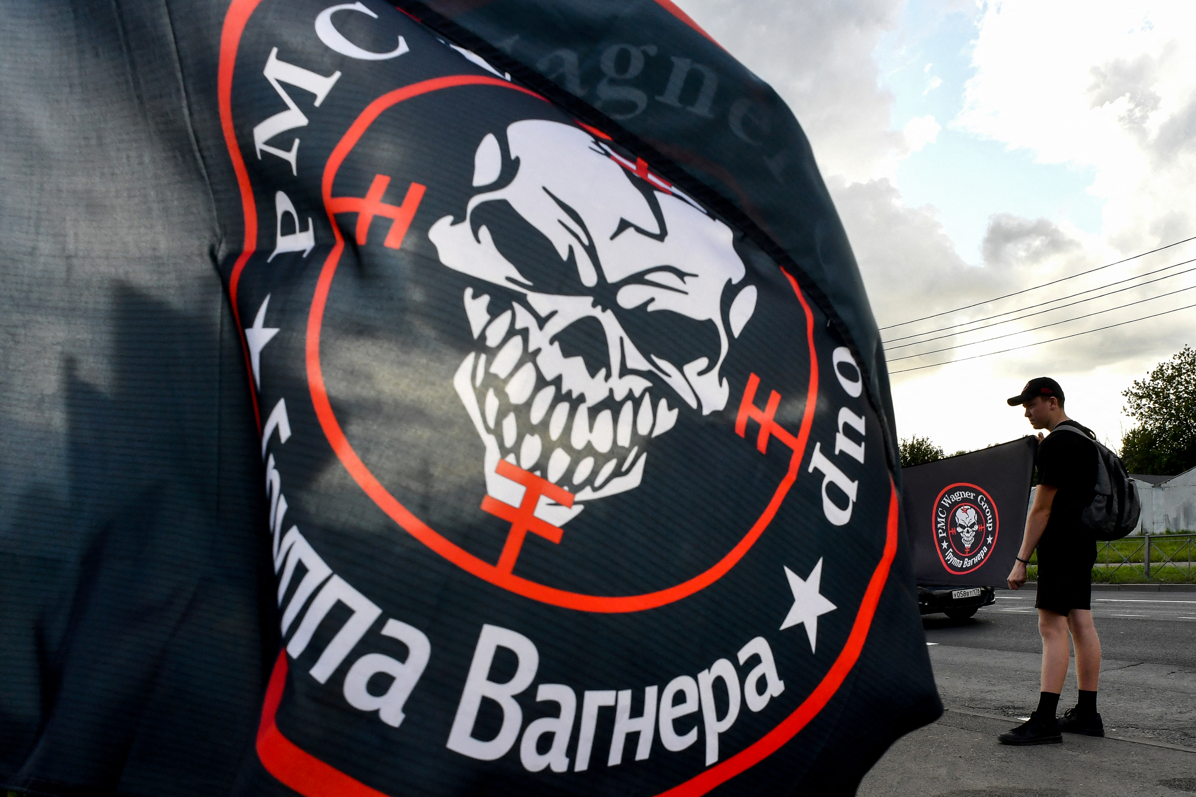Un hombre sostiene una bandera con el logotipo del grupo mercenario privado Wagner mientras otra bandera ondea al viento en un monumento improvisado a Yevgeny Prigozhin frente al Centro Wagner de la Compañía Militar Privada (PMC) en San Petersburgo, el 25 de agosto de 2023.
