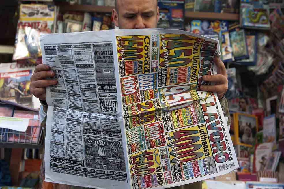Un hombre de Nápoles (Italia) busca trabajo en los avisos clasificados del periódico. / AFP