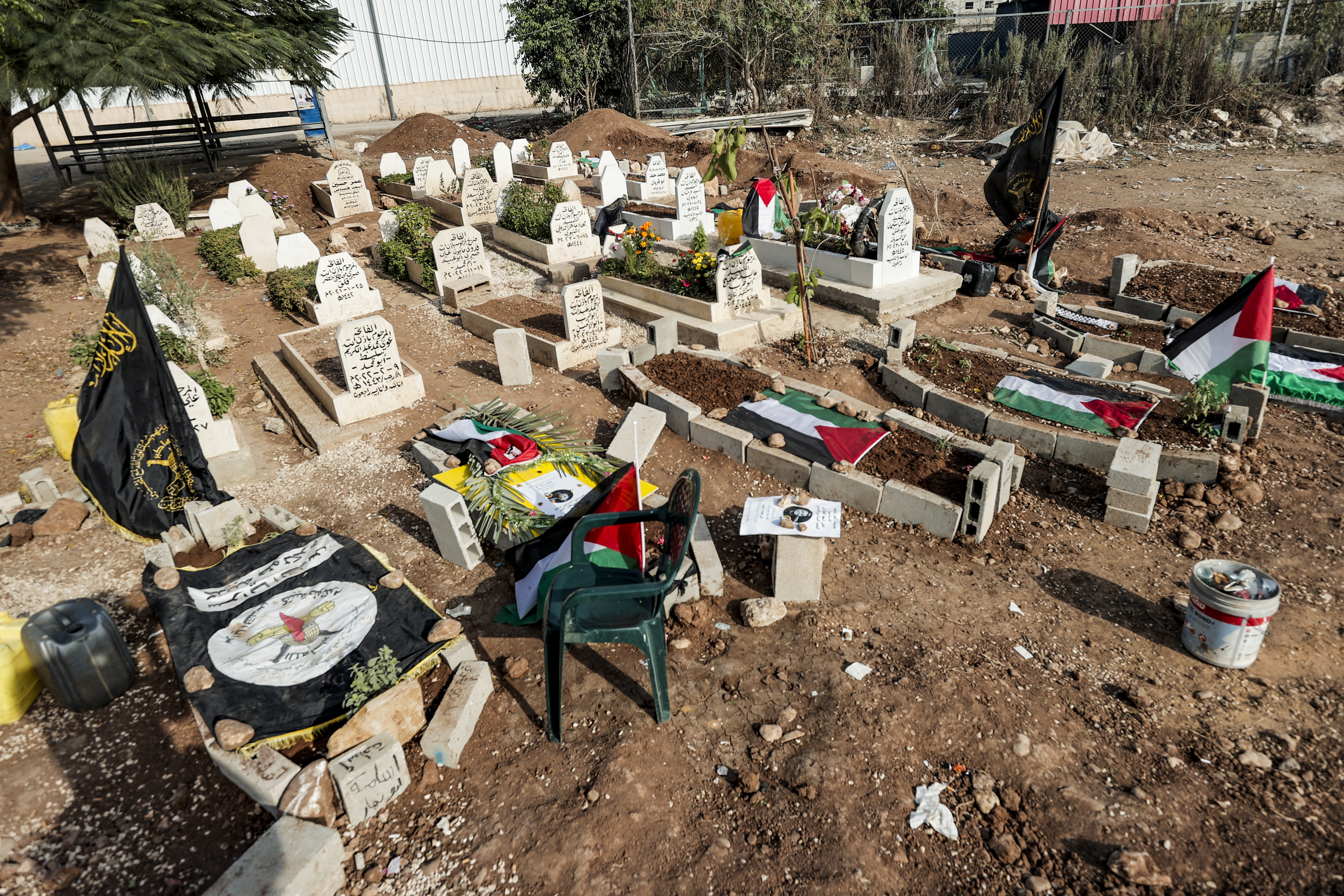 TULKAREM (GAZA Y CISJORDANIA), 23/10/2023.- Fotografía este lunes de tumbas pertenecientes a los fallecidos durante la incursión isaraelí en el campo de refugiados ocurrida entre el jueves y el viernes, cubiertas con banderas del grupo Yihad Islámica, de Palestina y de la brigada de Tulkarem, en Tulkarem (Cisjordania). El campo de refugiados palestinos de Nur Shams, cerca de Tulkarem, está viviendo las jornadas de mayor violencia en décadas, como otras partes de Cisjordania ocupada, donde las hostilidades con el Ejército israelí y los colonos han escalado tras el inicio de la guerra entre Hamás e Israel el pasado 7 de octubre. En el cementerio de Nur Shams la tierra todavía no está asentada en diez tumbas, cubiertas con banderas palestinas y del grupo Yihad Islámica, al que pertenecían los fallecidos entre el jueves y el viernes pasado en el campo, que se convirtió en una ratonera durante las 27 horas que duró una dura incursión de soldados israelíes. EFE/ Manuel Bruque