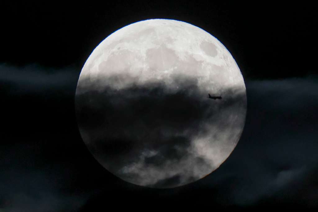 SANTIAGO DE COMPOSTELA, 17/10/2024.- La luna llena de este mes de octubre, conocida como la superluna del cazador, vista hoy jueves mientras pasa por delante un avión, desde Santiago de Compostela. EFE/Lavandeira Jr