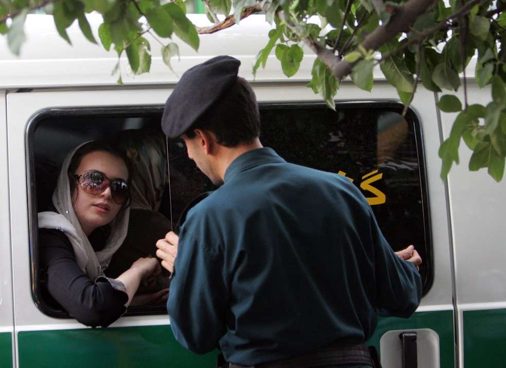Un policía iraní habla con una mujer sentada en un coche de policía después de que fue arrestada por su ropa "inapropiada".