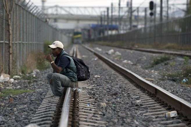 Un migrante sentado sobre una ferrovía prende un cigarrillo.
