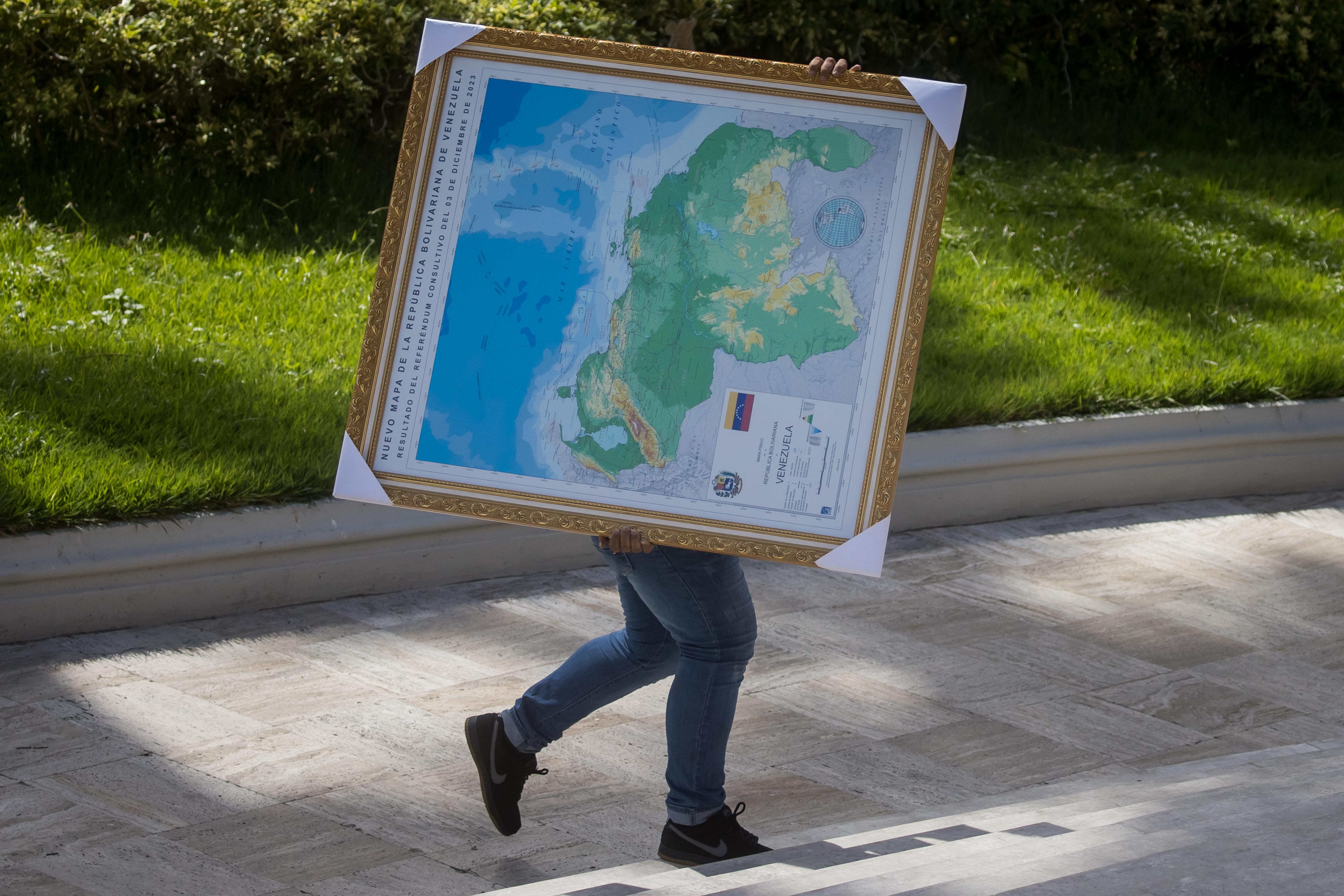-FOTODELDÍA- AME2481. CARACAS (VENEZUELA), 06/12/2023.- Un hombre carga hoy un cuadro del mapa de Venezuela con la adhesión del Esequibo, en uno de los jardines del Palacio Federal Legislativo en Caracas (Venezuela). La Asamblea Nacional (AN, Parlamento) de Venezuela, controlada por el chavismo, prevé aprobar dentro de una semana la ley de anexión del territorio en disputa con Guyana, en cumplimiento del referendo unilateral celebrado el domingo relacionado con este conflicto, aseguró el presidente de la Cámara, Jorge Rodríguez. EFE/ MIGUEL GUTIERREZ