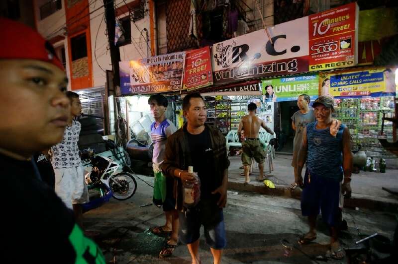 Un agente público vestido de civil sostiene una botella de licor incautada a un grupo de hombres que beben junto a la calle en Manila, Filipinas. / AP