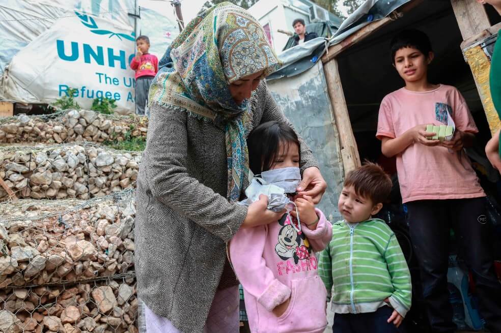 Una mujer ayuda a un niño con una máscara después de que miembros de la ONG "Team Humanity" entregaron máscaras faciales protectoras hechas a mano a migrantes y refugiados en el campamento de Moria en la isla de Lesbos el 28 de marzo de 2020. / AFP