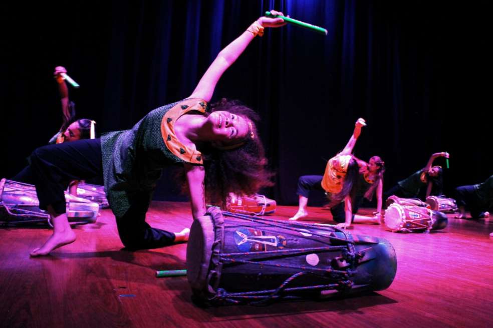 Niña bailando en un escenario. Sobre el suelo, y a su lado, hay un tambor. Parece un show de danza y percusión.