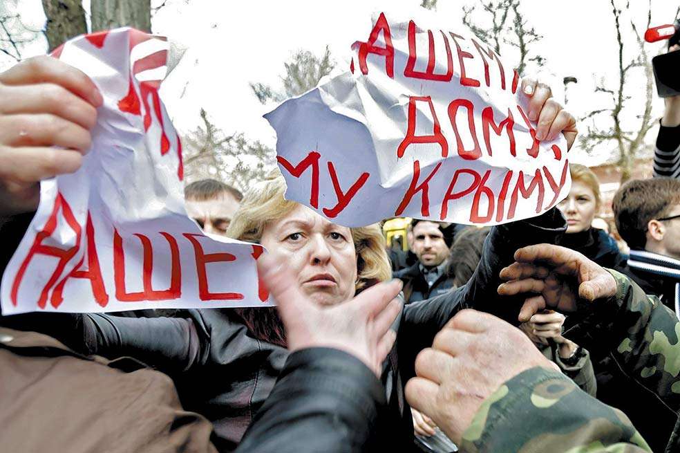 Unos hombres rompen un cartel que sostiene una manifestante, en el que se lee “Paz para nuestro hogar, Crimea”. / EFE
