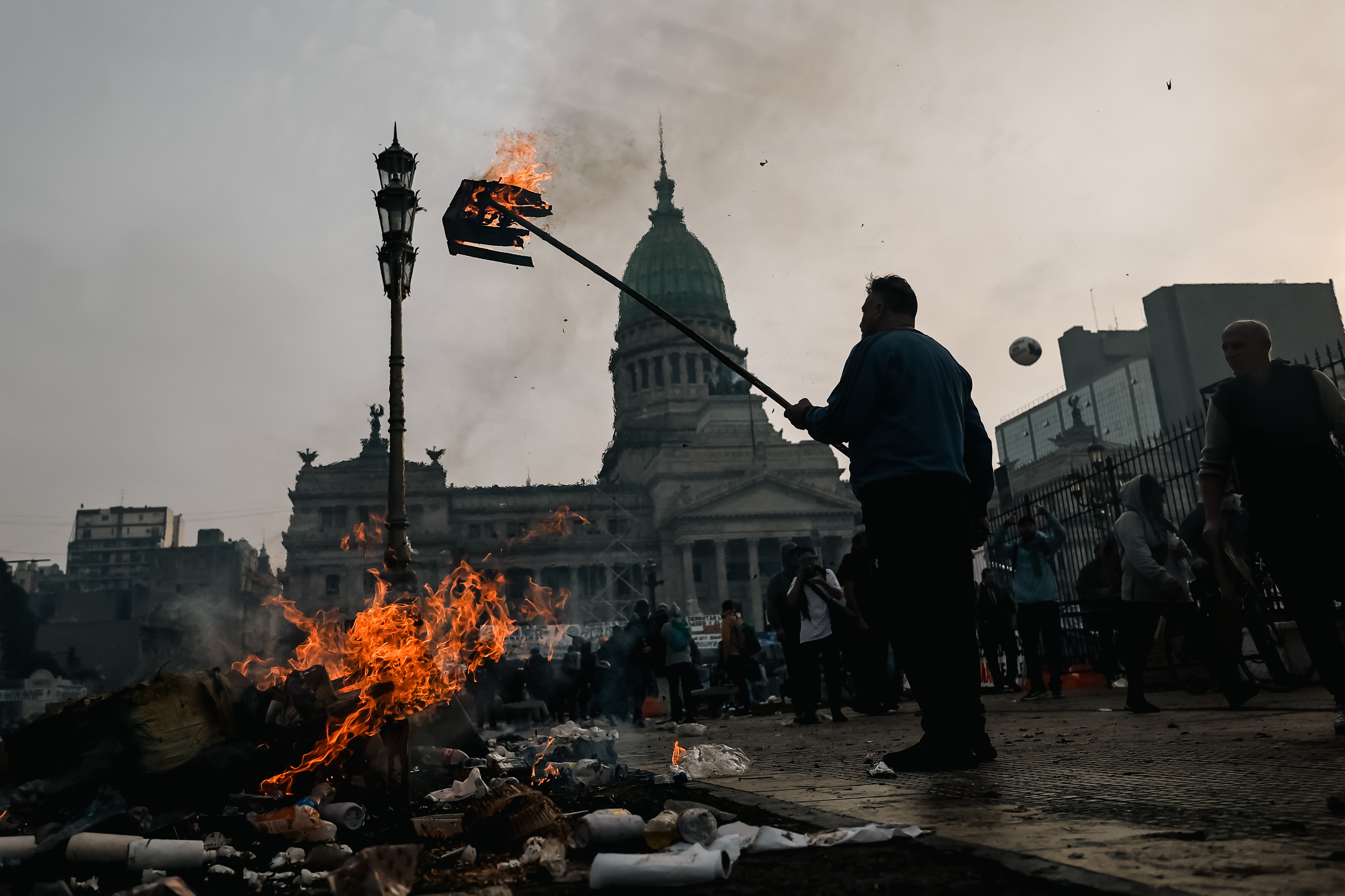 AME3498. BUENOS AIRES (ARGENTINA), 12/06/2024.- Un hombre quema una caja durante enfrentamientos entre la policía y personas que protestan a las afueras del senado durante un debate este miércoles, en Buenos Aires (Argentina). Manifestantes y policías protagonizan un choque este miércoles a las puertas del Senado de Argentina mientras la cámara legislativa debate la ley de Bases, el proyecto estrella del Gobierno, con el que el presidente Javier Milei pretende implementar un paquete de reformas económicas de gran calado. EFE/ Juan Ignacio Roncoroni