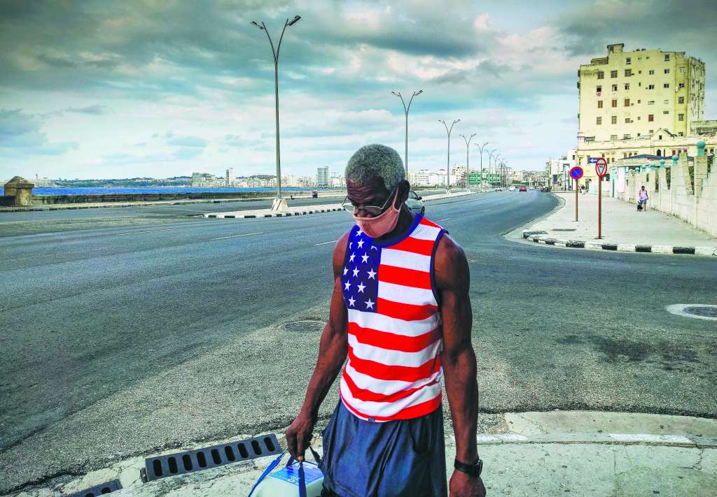 Un hombre con una camiseta que lleva la bandera de Estados Unidos camina por el malecón de La Habana, uno de los estandartes de la capital cubana.