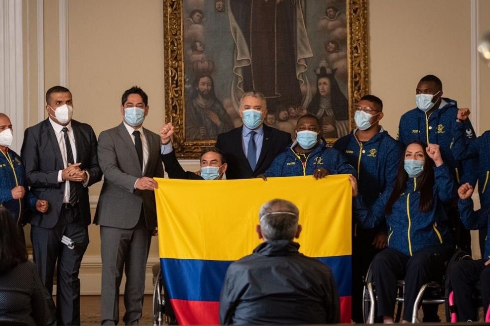 Iván Duque y Guillermo Antonio Herrera, nuevo ministro de deporte, sostienen la bandera que le entregaron a los abanderados paralímpicos, Érica Castaño y Francisco Palomeque.