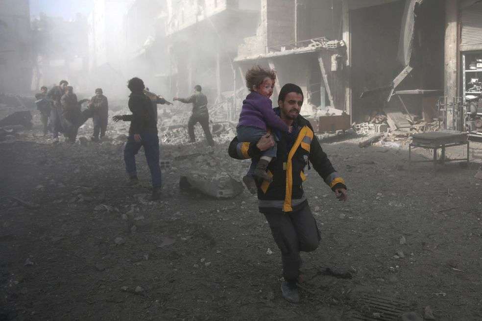 Un hombre, y su hija herida, tratan de huir de un bombardeo en Guta. / AFP