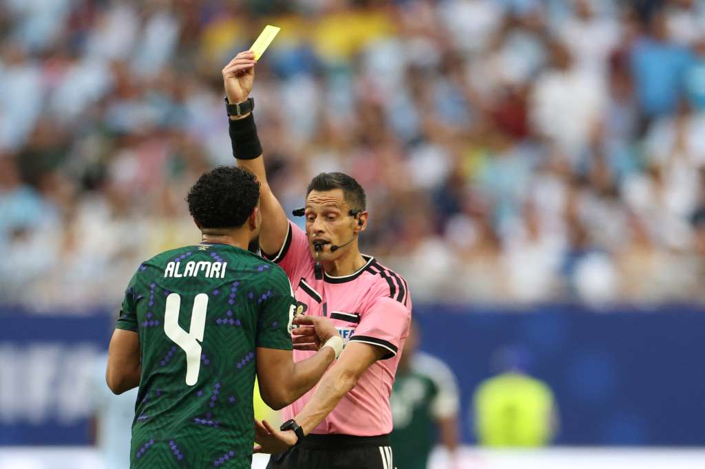 Italian referee Maurizio Mariani shows a yellow card to Saudi Arabia's defender #04 Abdulelah Al-Amri during the 2026 World Cup Group H football match between Saudi Arabia and Uruguay at the Miami Stadium in Miami Gardens on June 15, 2026. (Photo by PATRICIA DE MELO MOREIRA / AFP)