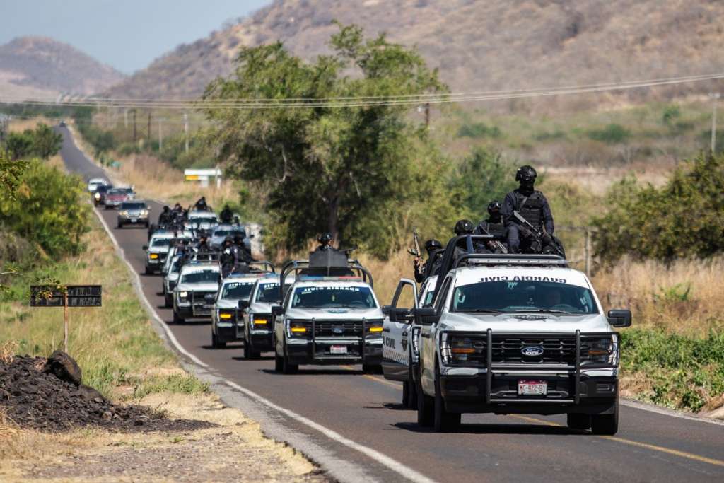 Members of the Civil Guard of Michoacan patrol a highway supported by armored vehicles after a wave of violence in the town of Aguililla, the birthplace of drug kingpin Nemesio Oseguera, leader of the Jalisco New Generation Cartel (CJNG) in Tierra Caliente, Mexico, on February 24, 2026. Mexican President Claudia Sheinbaum on February 24 dismissed risks to fans visiting Guadalajara, one of the venues for the 2026 World Cup, after a drug cartel riot caused fear in the city and much of the country on February 22. (Photo by Enrique Castro / AFP)