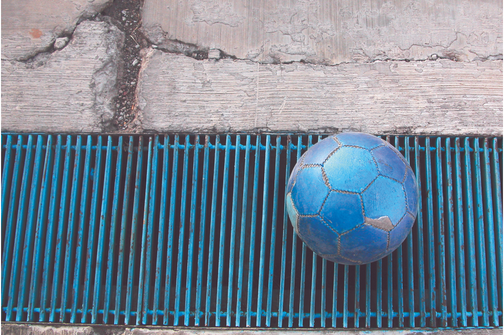 Balón de fútbol azul sobre el andén de una calle.