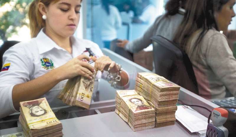 Una trabajadora de un banco manipula billetes de 100 bolívares, que perderán su valor y dejarán de circular desde hoy. / EFE