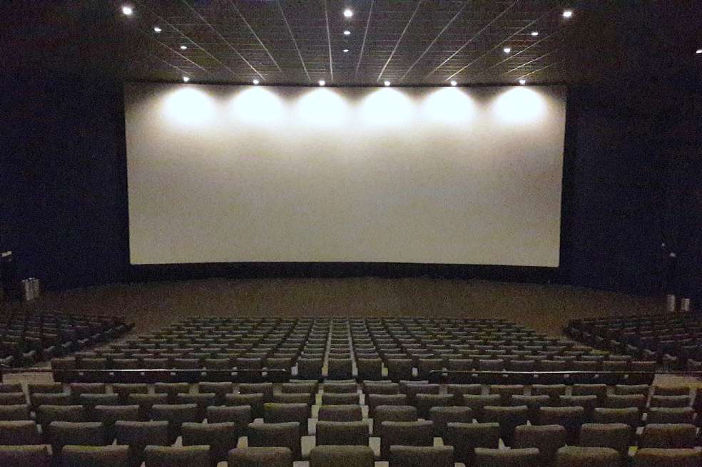 Sala de cine vacía. La pantalla está apagada.