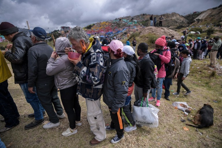Varias personas haciendo fila. Un hombre comen de una tasa
