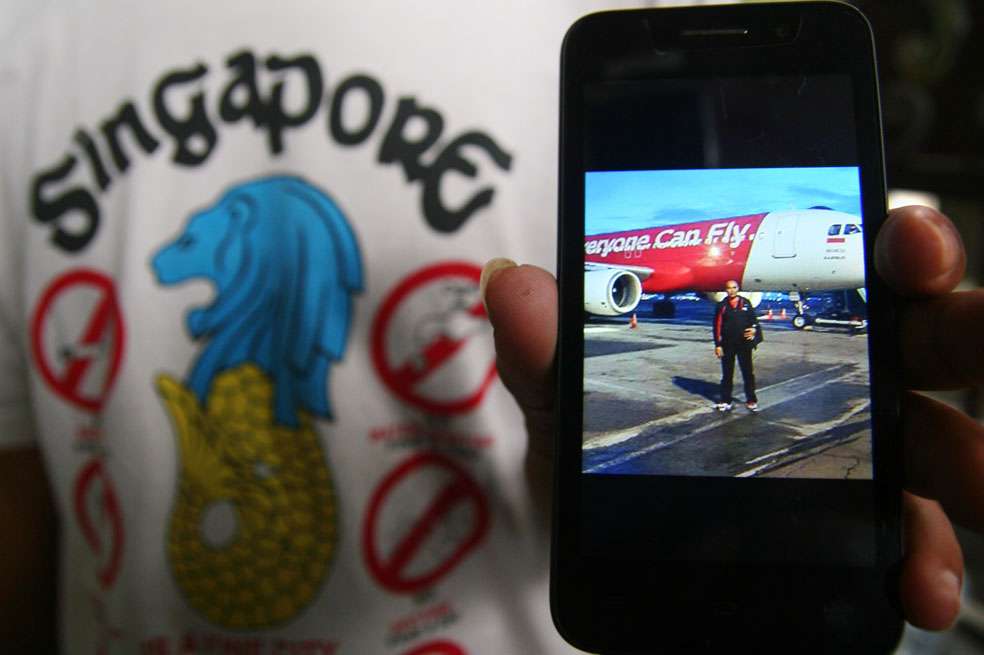 Un familiar de uno de los 162 pasajeros que viajaban en el vuelo QZ8501 de AirAsia muestra una foto del viajero antes de subirse al avión desaparecido. / AFP