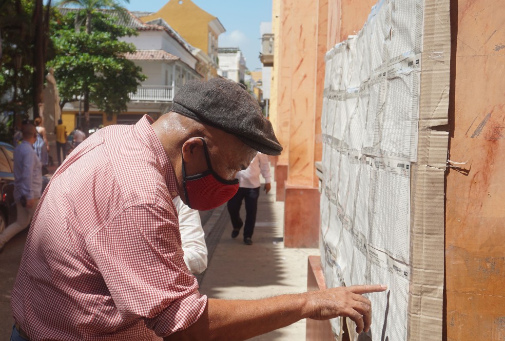 En una mañana soledad en Cartagena, un adulto mayor de camisa corta constata la mesa de votación en la que deberá sufragar en la primera vuelta de le lección presidencial.