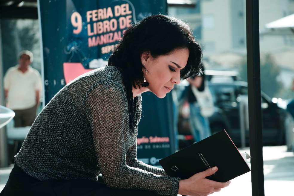 Lucía Estrada en la novena Feria de Manizales. La poeta está sentada leyendo un libro.