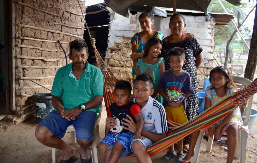 Los ocho miembros de la familia Olmos, dos de ellos sentaos en una hamaca frente a su pequeña casa.