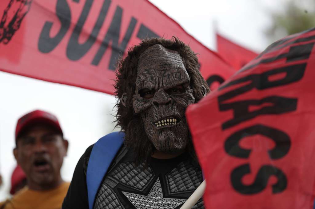 AME3732. CIUDAD DE PANAMÁ (PANAMÁ), 18/07/2022.- Un hombre enmascarado sostiene una bandera del gremio sindical Suntracs durante una protesta hoy, en Ciudad de Panamá (Panamá). Miembros del Sindicato Único Nacional de Trabajadores de la Industria de la Construcción y Similares de Panamá (SUNTRACS) protestan hoy cerrando los principales corredores de la capital panameña, en reclamos por el congelamiento del precio del combustible y la reducción de los costos de alimentos y medicamentos. El gremio docente reunido con el Gobierno rompió el acuerdo alcanzado el domingo con el Gobierno y acordó continuar la huelga y no césar la movilización en las calles. EFE/ Bienvenido Velasco