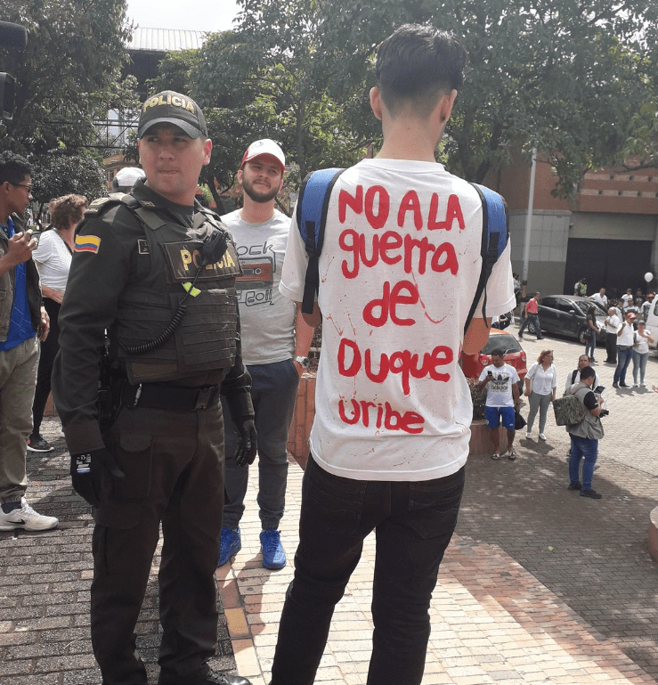 Joven de espaldas, con camisa que dice "No a la guerra de Duque-Uribe".