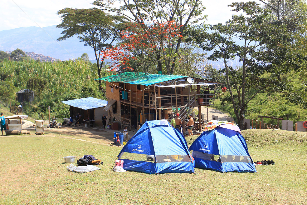 Un parque con dos carpas azules y una casa de madera en la Comuna 13 de Medellín.