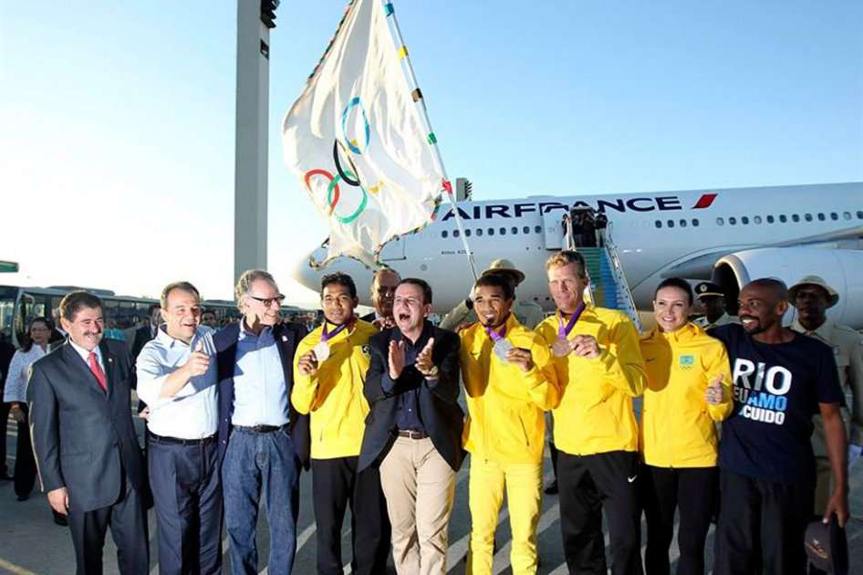 El alcalde de Río de Janeiro, Eduardo Paes, posa junto a unos atletas que ganaron medallas de plata y bronce en las olimpíadas de Londres 2012, a su llegada con la bandera olímpica. / EFE