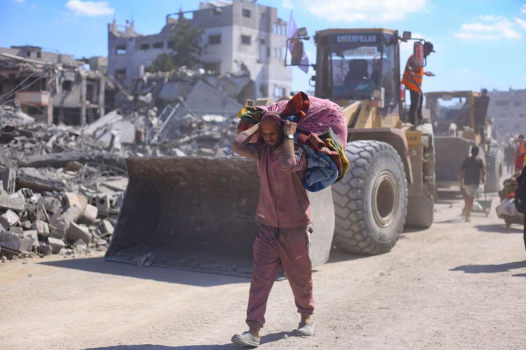 FOTODELDIA GAZA, 14/10/2025.- Un hombre con un hatillo con sus pertenencias pasa ante varias excavadoras del Ayuntamiento de la ciudad de Gaza que comienza este martes las operaciones de remoción de escombros y apertura de las calles principales de la capital gazatí para despejarlas y prepararlas para su uso, tras dos años de bombardeos. La reconstrucción de la Franja de Gaza, donde la destrucción es casi completa, requerirá al menos 70.000 millones de dólares, de los cuales 20.000 millones deben ser invertidos en los próximos tres años para hacer viable la vida en este territorio palestino. EFE/ Ahmad Awad