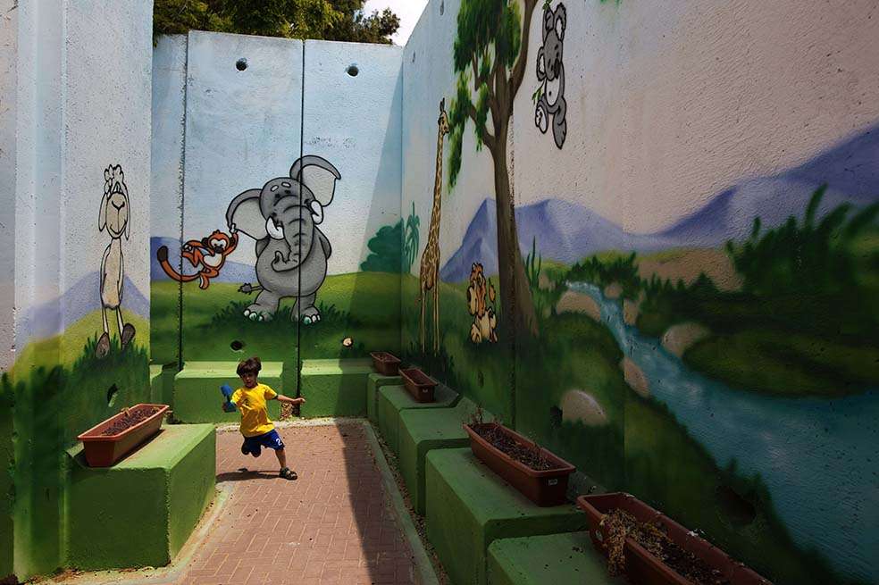 Un niño juega en un jardín cerca del borde israelí con la Franja de Gaza: los muros están reforzados para proteger contra bombardeos. / AFP