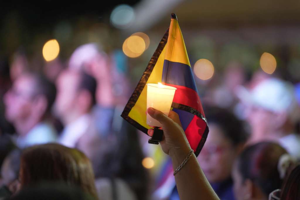 AME3260. CALI (COLOMBIA), 24/08/2025.- Una persona sostiene una bandera de Colombia y una vela encendida en una 'velatón' por la paz y la memoria este domingo, frente a la Base Aérea Marco Fidel Suárez, en Cali (Colombia). Centenares de personas, vestidas de blanco y con velas en mano, se reunieron en el lugar del atentado que el jueves sacudió a la ciudad colombiana en memoria de los seis civiles que murieron en la explosión de un camión bomba. EFE/ Ernesto Guzmán