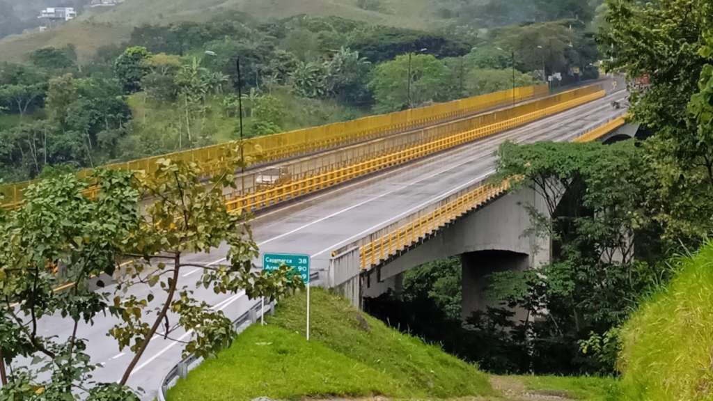Puente rodeado de plantas, vacío y sin automóviles que le rodeen, mojado por la lluvia que recién acaba de escampar.
