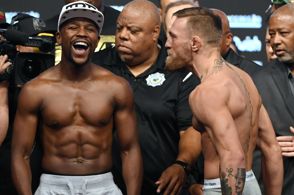 El boxeador Floyd Mayweather Jr. (L) se ríe después de discutir con el campeón de peso ligero de UFC, Conor McGregor, durante el pesaje oficial. / AFP