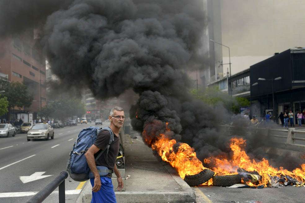 Un hombre intenta pasar una barricada instalada en una de las principales vías de Caracas, escena que se repite a diario en la capital venezolana. / AFP