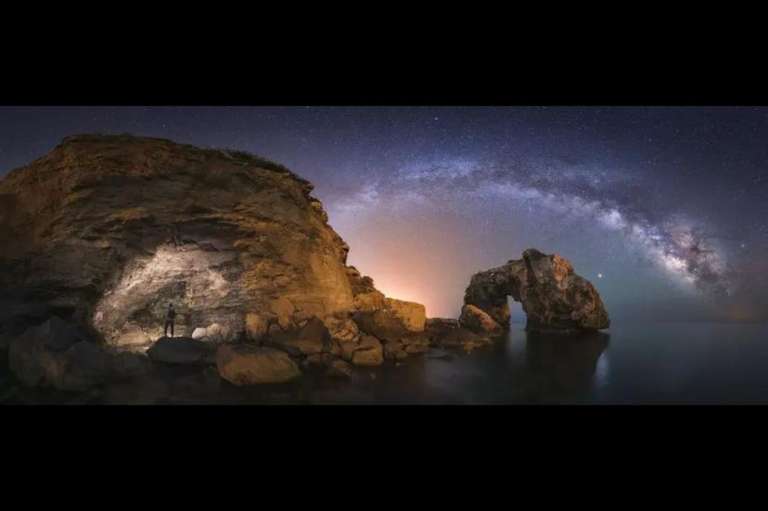 Mundo nocturno:
Marco Marco tomó una fotografía nocturna panorámica en la que pude captar el arco de la Vía Láctea pasando por detrás del arco natural llamado Es Pontás.