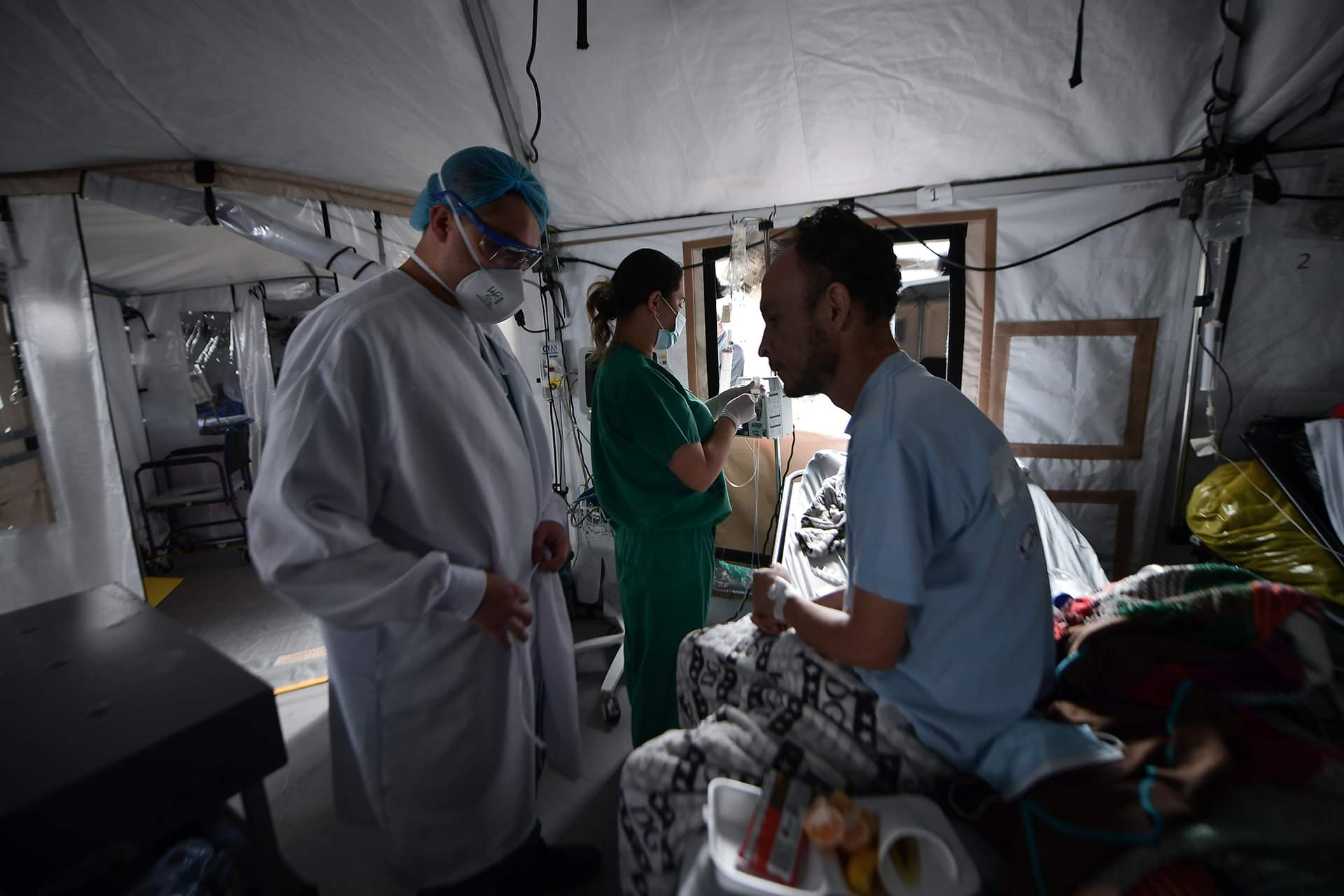 Un médico revisando a un paciente, mientras una enfermera revisa el suero