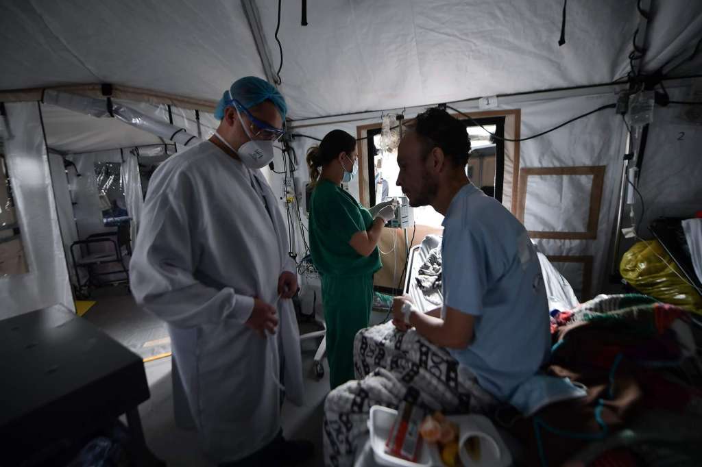 Un médico revisando a un paciente, mientras una enfermera revisa el suero
